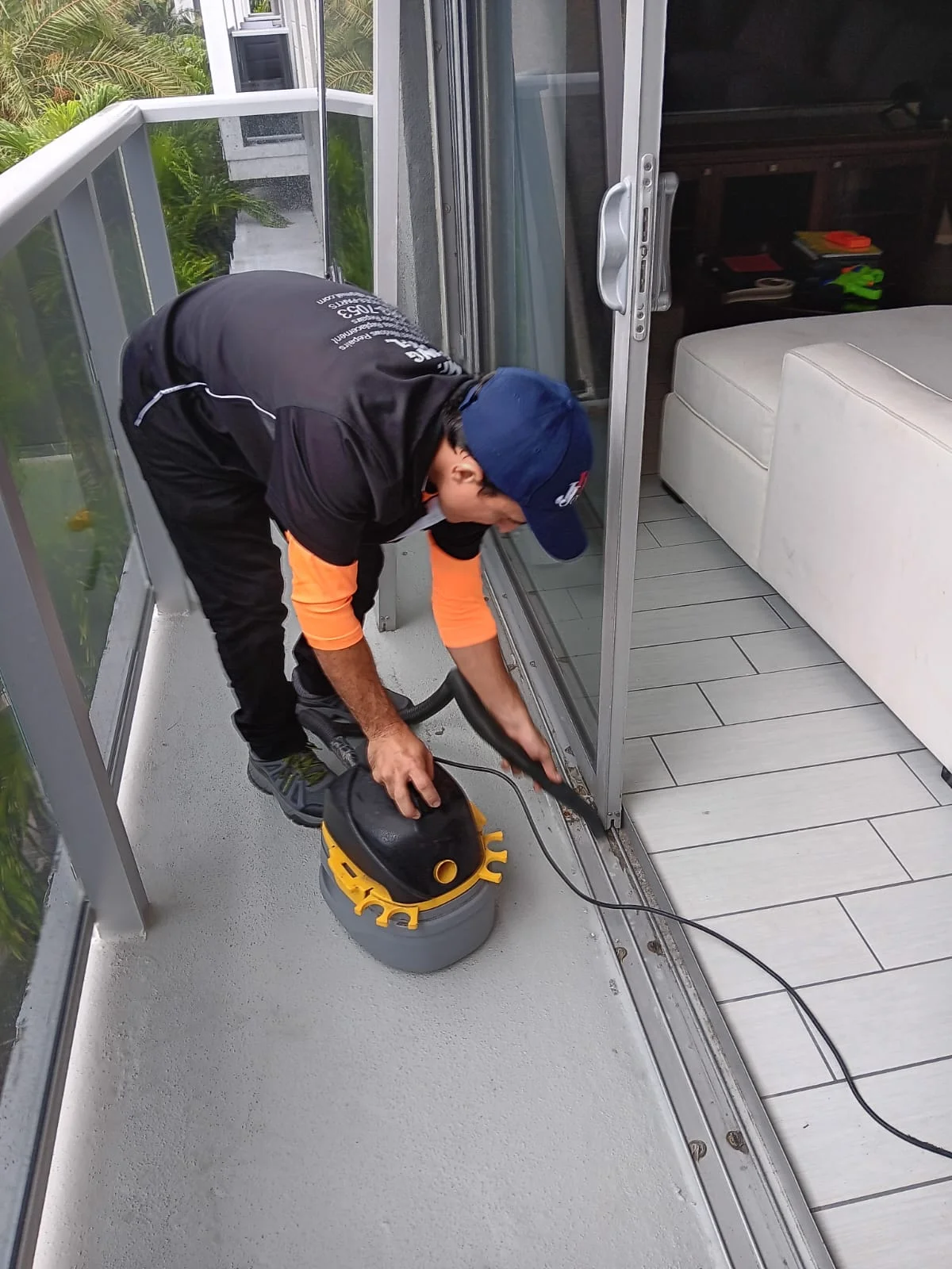 Technician cleaning a sliding door track with a vacuum on a balcony